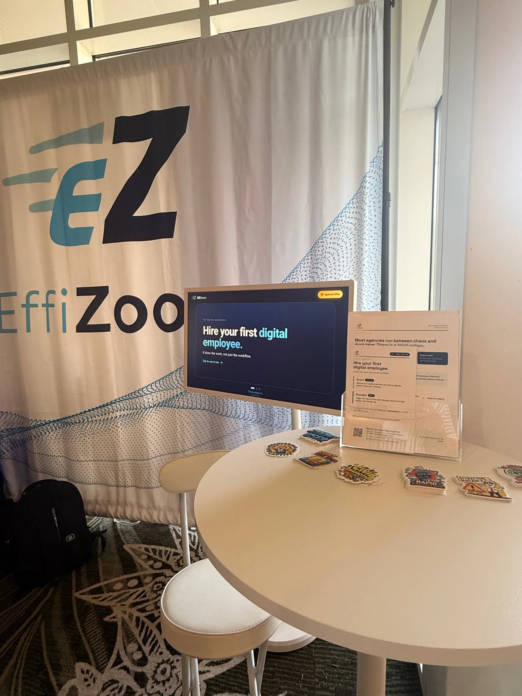 The EffiZoom booth: banner, a demo screen reading Hire your first digital employee, and a table of stickers
